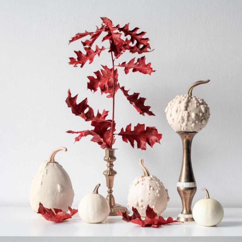 białe dynie i jesienne liście na złotych wazonikach i świecznikach