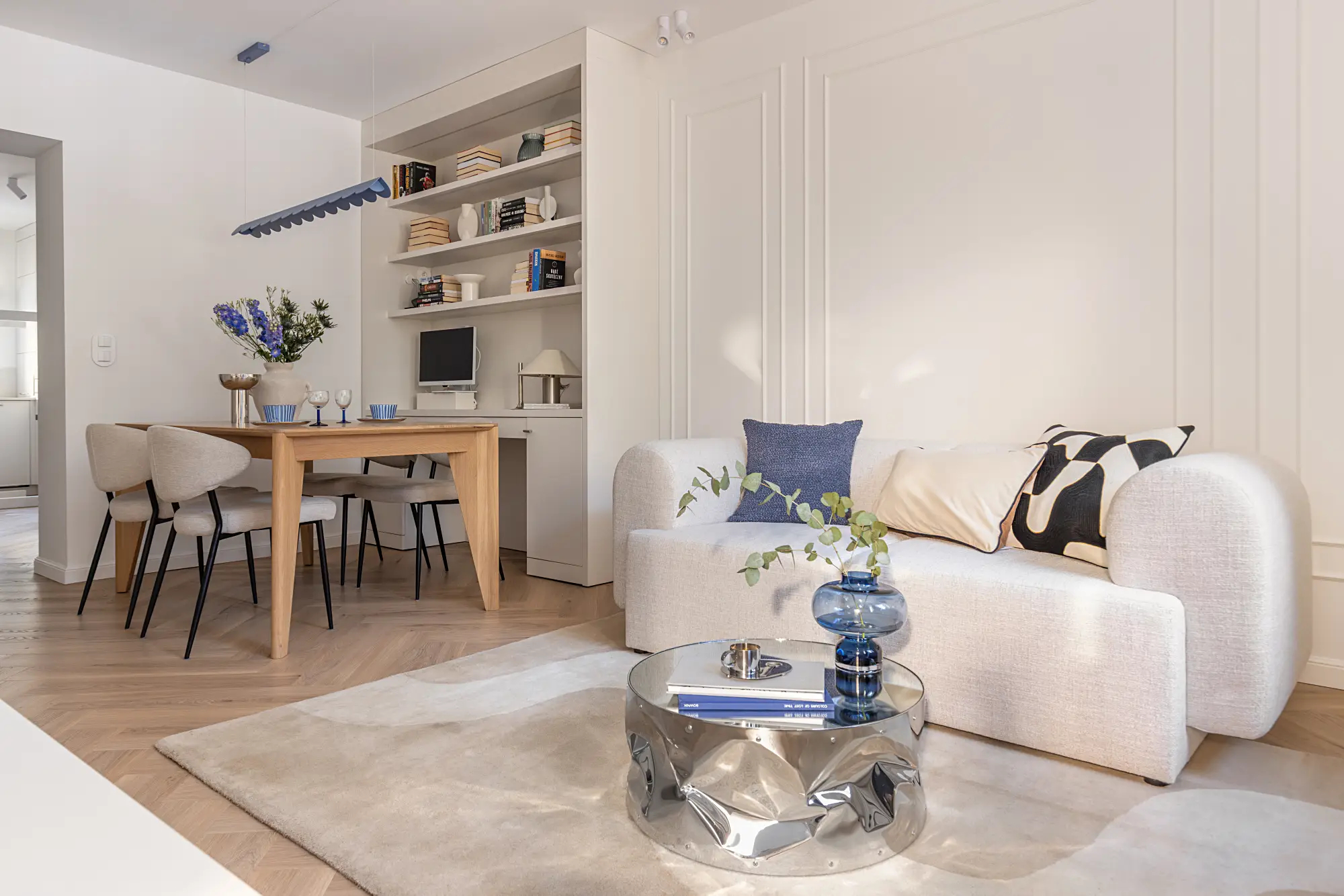 Jasna, zaokrąglona sofa, lustrzany stolik kawowy i błękitne dodatki w salonie w mieszkaniu 60m2